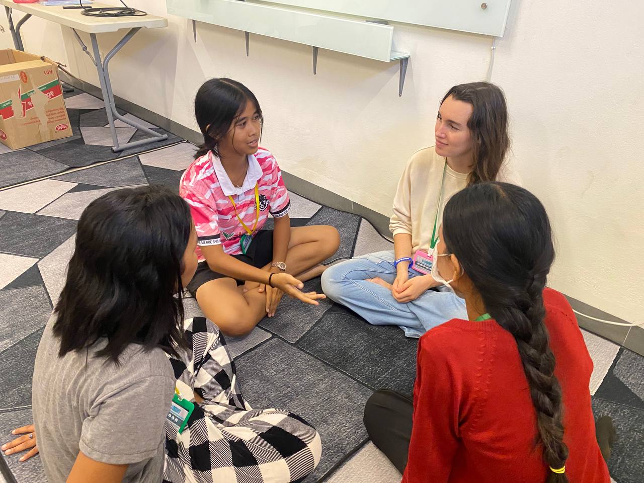 Brieya sitting cross-legged in a close conversation with three Cambodian girls.