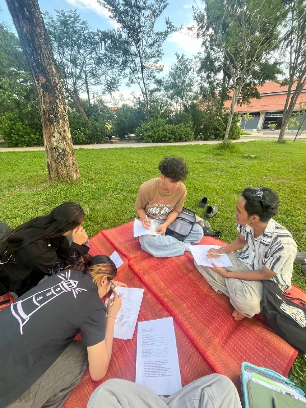 Brieya and teammates sitting on mats outdoors, writing and discussing notes together on a grassy campus.