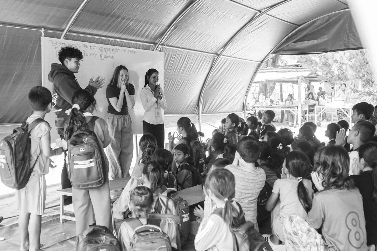 Brieya and a local teacher leading an English lesson at a whiteboard for a group of Cambodian students.