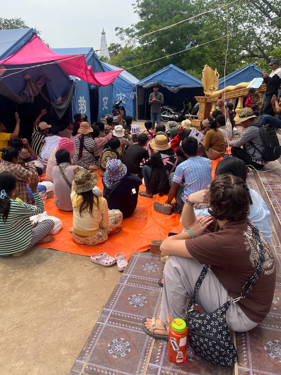 Brieya sitting among a Cambodian community gathered under tents during an outreach event.