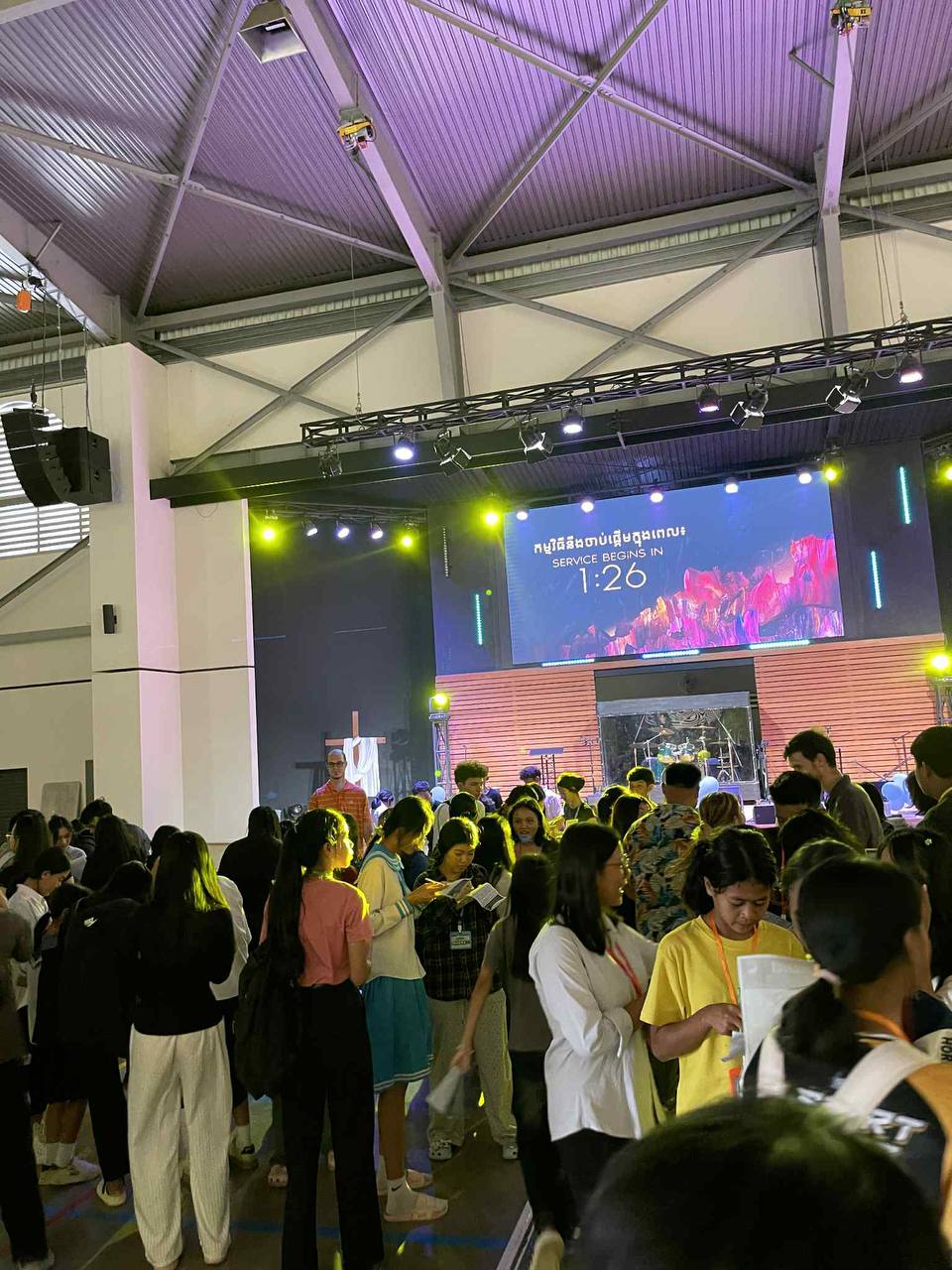 A crowd of youth gathered in a gymnasium before a service, countdown clock on the big screen.
